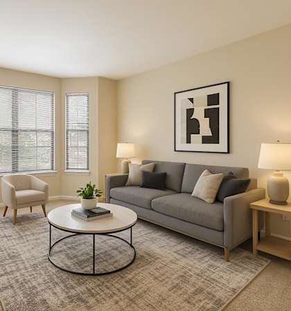 A living room with a grey couch, a white coffee table, and a large mirror on the wall.