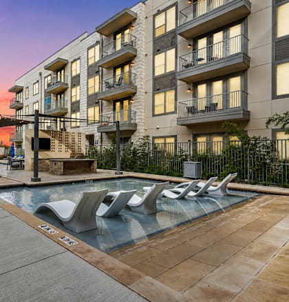 A sunset view of a pool area with lounge chairs and apartment buildings.