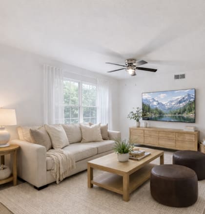 A living room with a white couch, a wooden coffee table, and a painting of a mountain landscape on the wall.