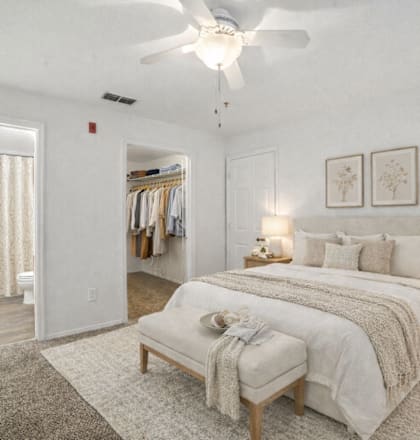 A bedroom with a large bed, a bench, and a ceiling fan.