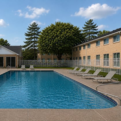 A large swimming pool in front of a building with a covered area and lounge chairs.