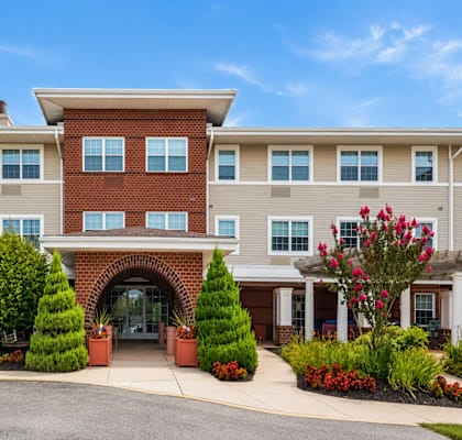 A large building with a red brick entrance and a landscaped front yard.