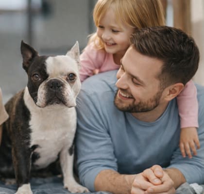 A family of three is lying down with a dog between them.