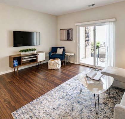 A living room with a grey couch, a blue chair, and a television on the wall.