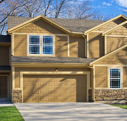 A two-story house with a garage door and a stone wall.
