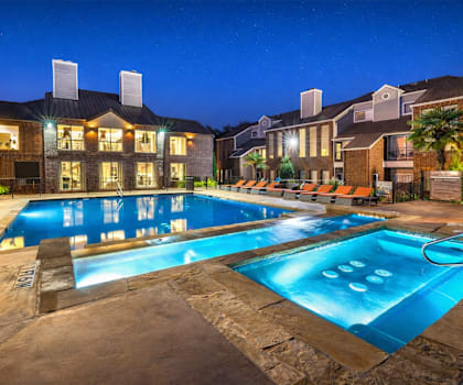 A large swimming pool in front of a building with lights on.