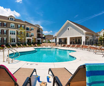 A large swimming pool surrounded by lounge chairs and umbrellas in front of a building.