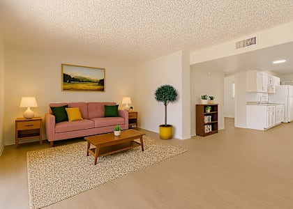A living room with a pink couch, a small tree, and a painting on the wall.