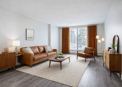 A living room with a brown leather sofa, a wooden coffee table, and a large window with orange curtains.