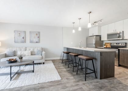 A modern kitchen with a white sofa and grey bar stools.