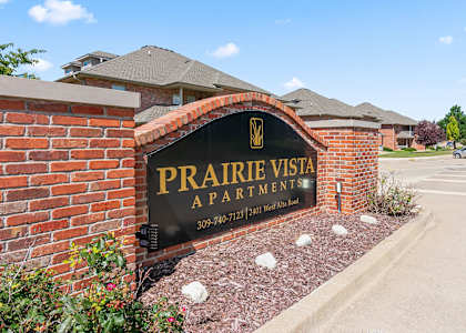 A sign for Prairie Vista Apartments is displayed in front of a brick wall.