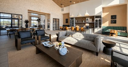 Spacious apartment resident lounge with high ceilings, comfortable seating, kitchen island, dining table, and natural light.