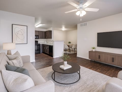 A living room with a grey couch, a coffee table, and a flat screen TV mounted on the wall.