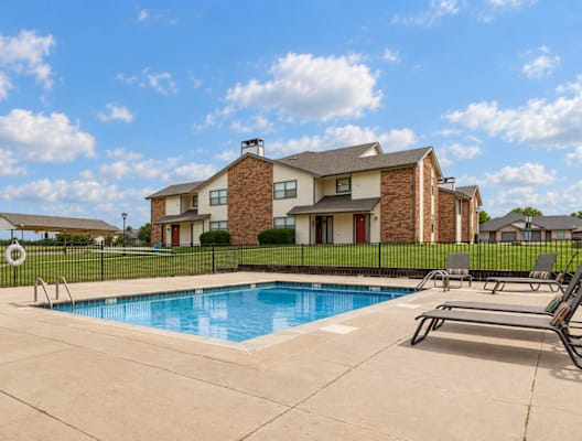 A swimming pool in front of a house with a black fence.