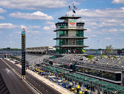 A view of a race track with a large building in the background and a crowd of people in the foreground.