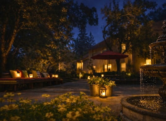 A beautifully lit garden at night with a fountain in the foreground.
