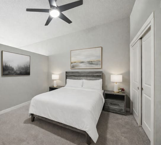 A bedroom with a bed, nightstands, and a ceiling fan.