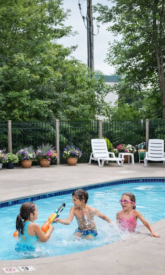 Three children playing in a pool surrounded by lounge chairs and greenery.