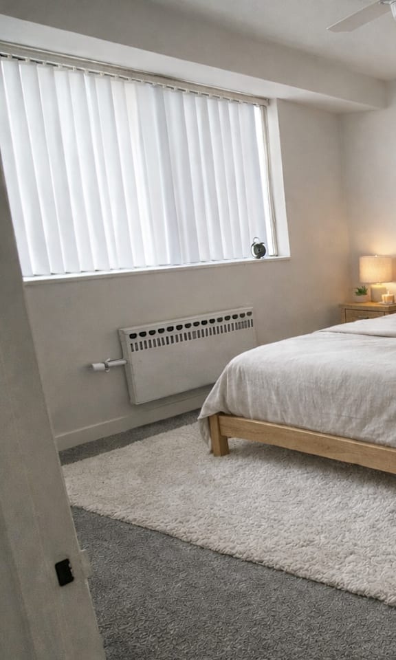A bedroom with a large bed, a ceiling fan, and a window with blinds.