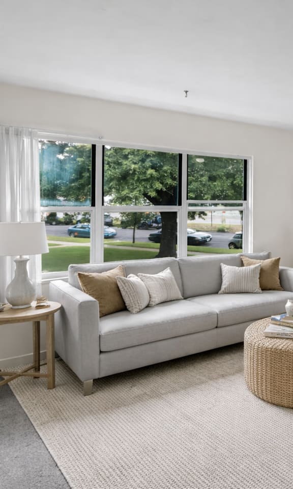 A living room with a grey couch, a round wicker table, and a grey rug.