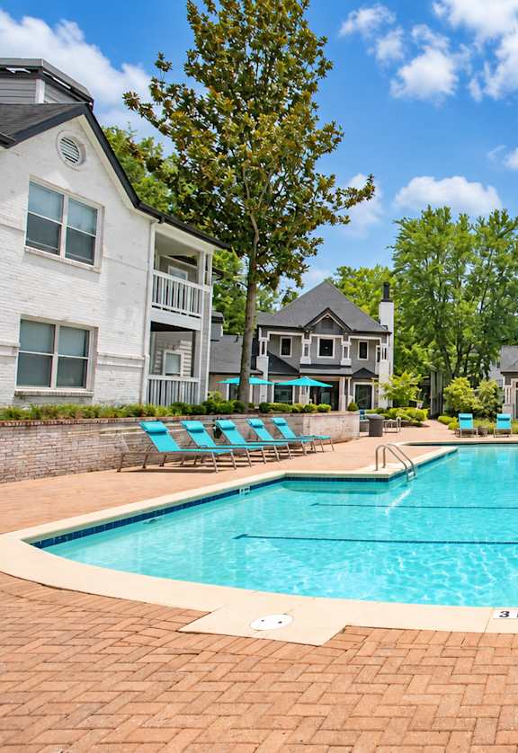A swimming pool surrounded by chairs and trees in a residential area.