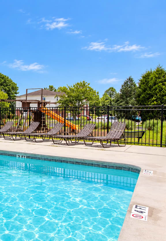 A swimming pool surrounded by a black fence and chairs.