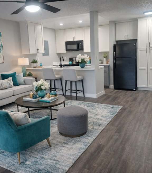 A kitchen with a black counter top and a teal kettle on a floral mat.