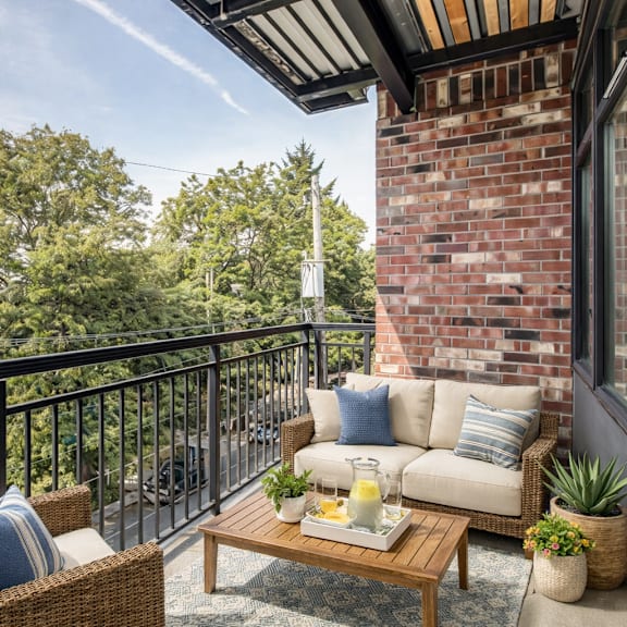 A balcony with a sofa, wicker chair, and a coffee table with a tray of food on it.