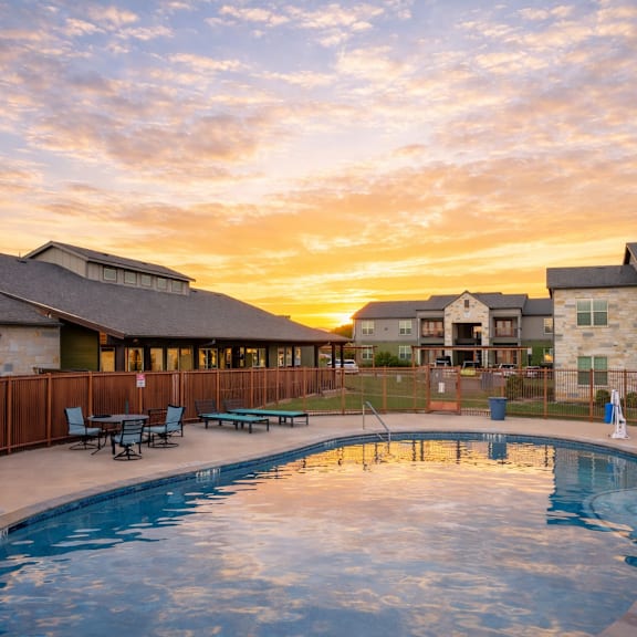 A swimming pool surrounded by a wooden fence and chairs.