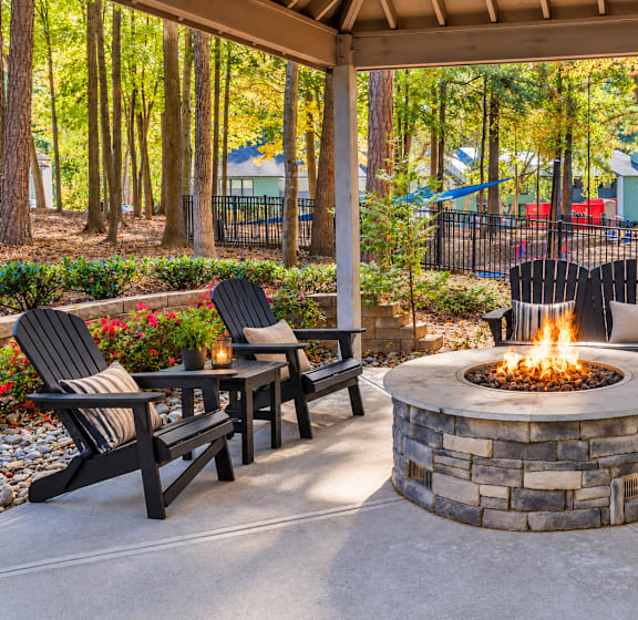 A fire pit is surrounded by black chairs and tables in a patio setting.
