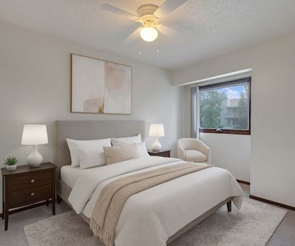 A cozy kitchen with white appliances, blue kitchen utensils, overhead lighting, light countertops with lots of room, a bar counter with wood and gray barstools, and large wooden cabinets at Russian Jack Apartment Homes. 