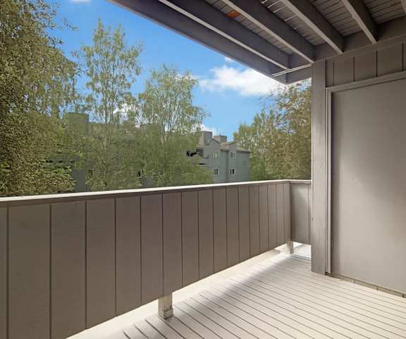 A wooden balcony with the door to the apartment and a gorgeous view of the other apartment buildings at Russian Jack Apartment Homes. 