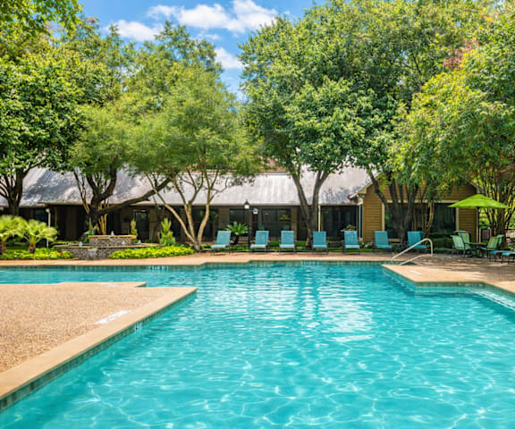 A large swimming pool surrounded by trees and chairs.