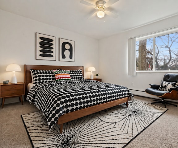 A bedroom with a black and white bedspread and a window showing a tree outside.