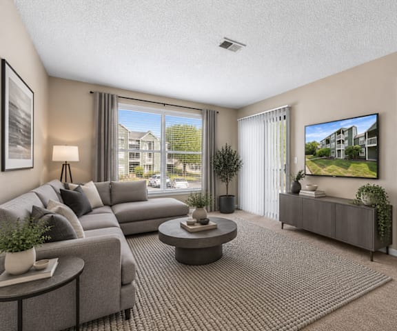 A living room with a grey couch, a coffee table, and a flat screen TV mounted on the wall.