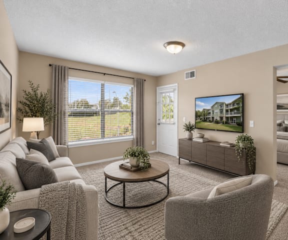 A living room with a grey couch, a coffee table, and a large window with a view of the outside.