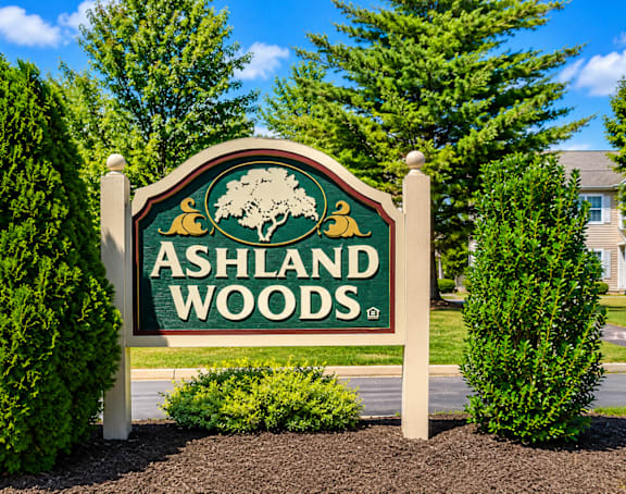 A sign for Ashland Woods is displayed in front of some trees.