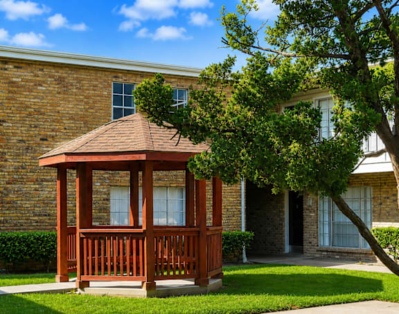 A gazebo sits in front of a brick building.