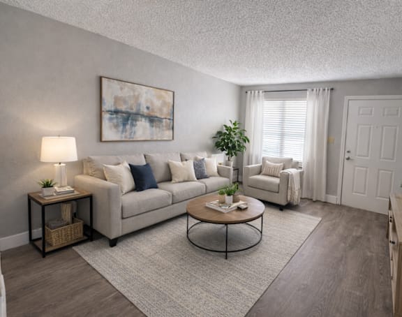 A living room with a grey couch, a coffee table, a lamp, a plant, and a painting on the wall.