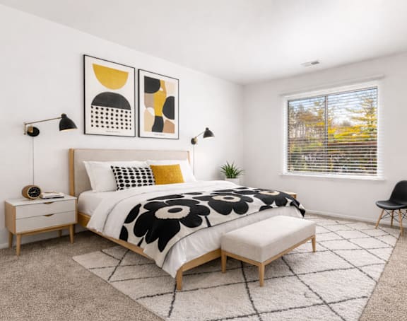 A bedroom with a large bed, a chair, and a window with blinds.