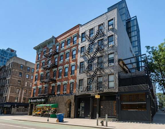 A modern building with a glass facade is situated next to a traditional brick building with a fire escape.
