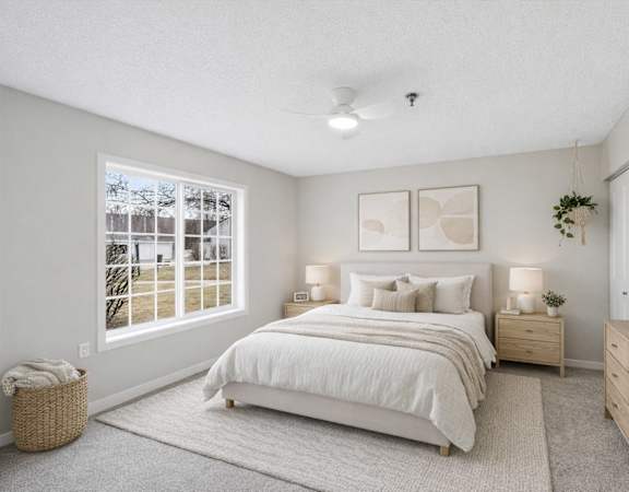 A bedroom with a large bed, nightstands, and a window with a view of a tree-lined street.