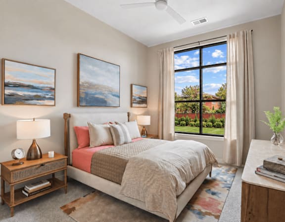 A bedroom with a large bed, a ceiling fan, and a view of the backyard through the window.