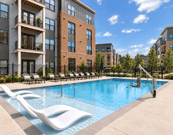 A pool surrounded by lounge chairs in front of apartment buildings.