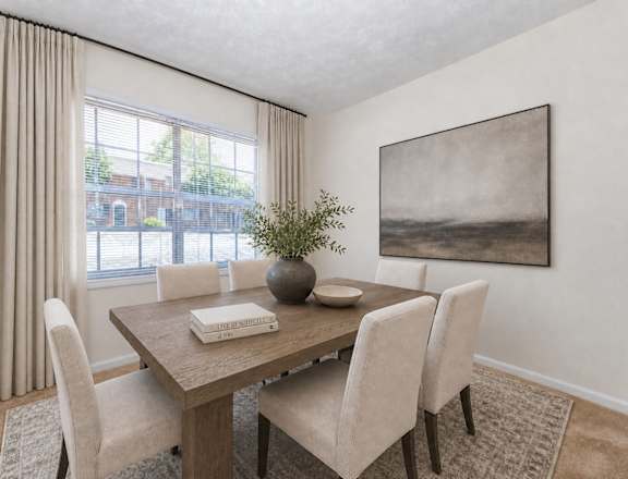 A dining room with a wooden table and chairs, a vase with a plant, and a framed picture on the wall.