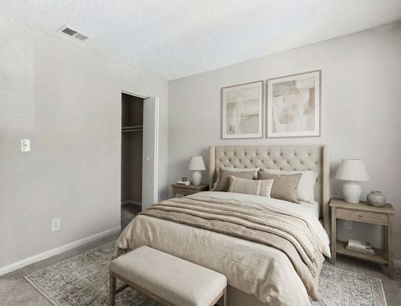 A bedroom with a large bed, a nightstand with lamps, a chair, and a wardrobe.