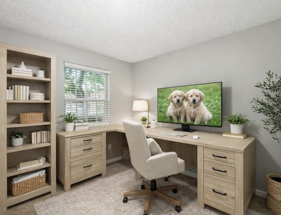 A room with a desk, chair, and a TV displaying two dogs.