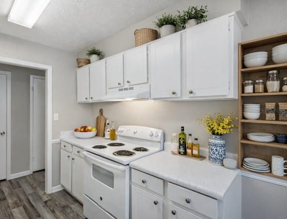 A white kitchen with a sink, stove, and cabinets.