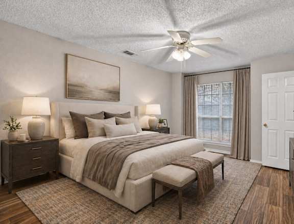 A bedroom with a large bed, a ceiling fan, and a painting on the wall.