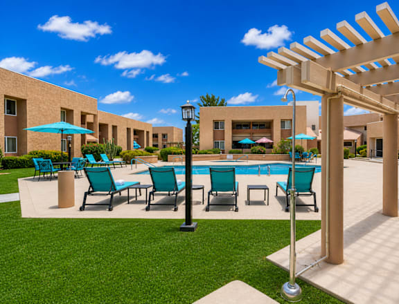 A pool surrounded by chairs and umbrellas with a building in the background.